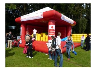 Eine rote Hüpfburg mit Menschen darin und darum.